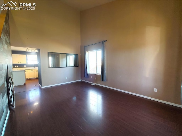 unfurnished living room featuring dark wood-style floors, a high ceiling, and baseboards