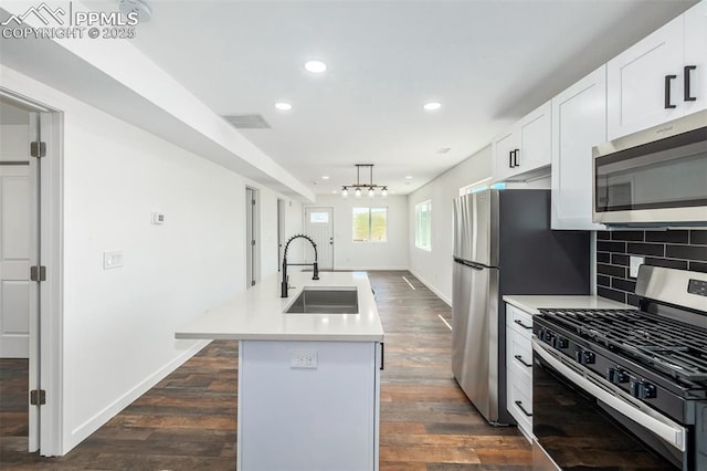 kitchen with stainless steel appliances, tasteful backsplash, dark wood-type flooring, a kitchen island with sink, and a sink