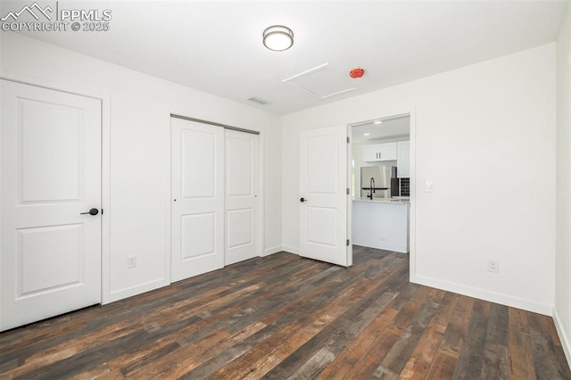 unfurnished bedroom featuring attic access, visible vents, dark wood finished floors, freestanding refrigerator, and a closet