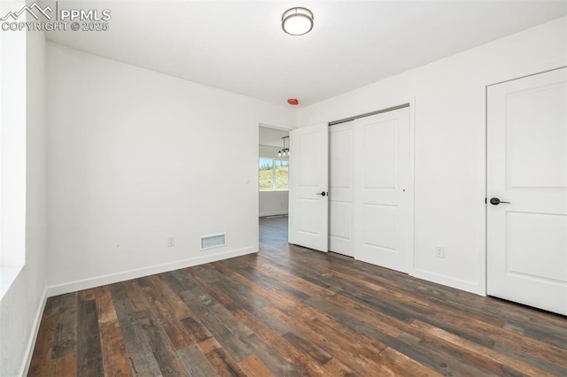 unfurnished bedroom with baseboards, visible vents, dark wood finished floors, and a closet