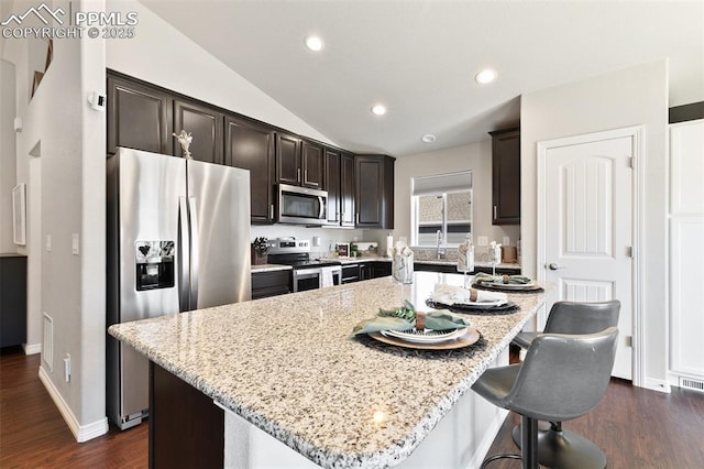 kitchen with stainless steel appliances, lofted ceiling, dark brown cabinets, and light stone counters