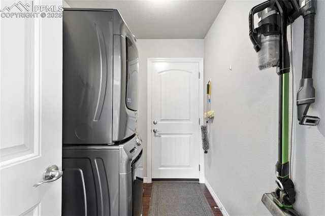 laundry area featuring stacked washer / drying machine, laundry area, dark wood finished floors, and baseboards