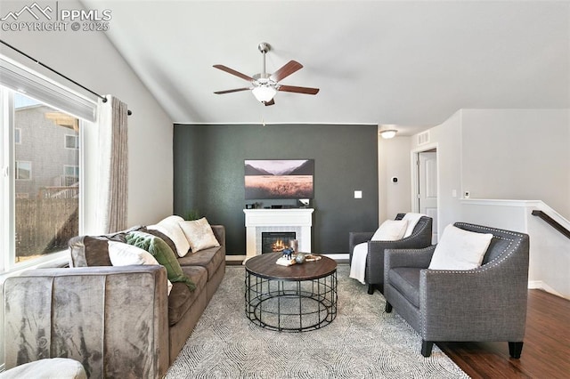 living area featuring lofted ceiling, visible vents, a ceiling fan, a glass covered fireplace, and wood finished floors