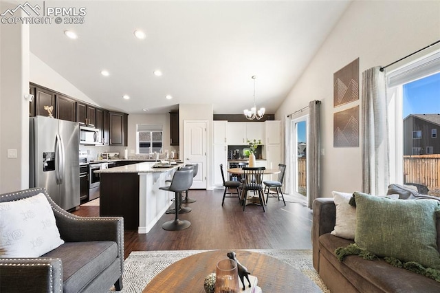 living room with vaulted ceiling, plenty of natural light, dark wood finished floors, and a notable chandelier