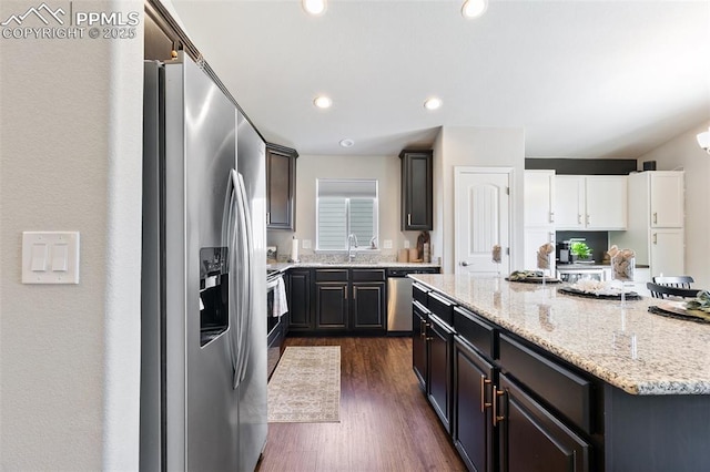 kitchen with dark wood-style floors, light stone counters, a center island, stainless steel appliances, and recessed lighting