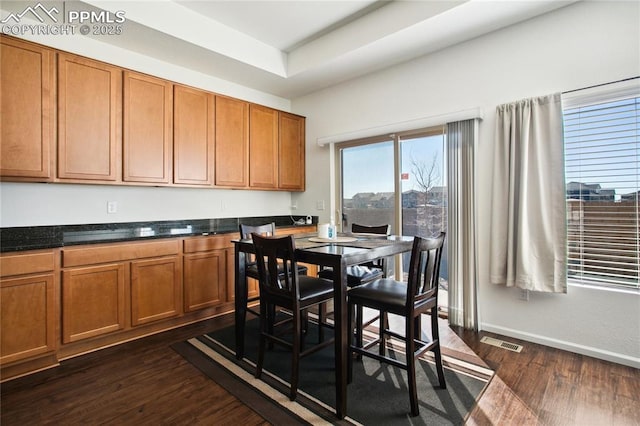 dining room with dark wood-style floors, a tray ceiling, visible vents, and baseboards