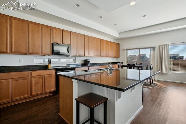 kitchen with brown cabinetry, dark countertops, black microwave, and a sink