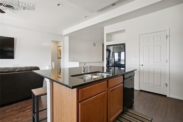 kitchen featuring dark stone counters, an island with sink, open floor plan, black appliances, and a sink