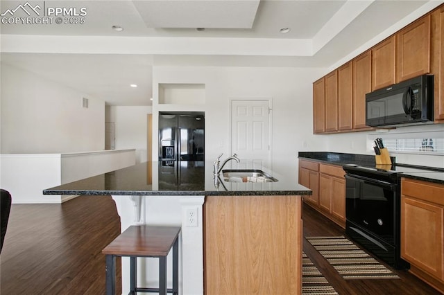 kitchen with a breakfast bar, dark stone counters, a sink, dark wood-style floors, and black appliances