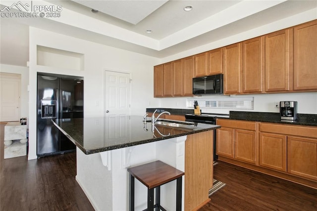 kitchen with dark wood-style flooring, brown cabinetry, a sink, dark stone countertops, and black appliances