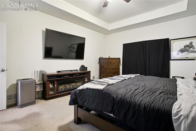 carpeted bedroom with ceiling fan, a raised ceiling, and visible vents