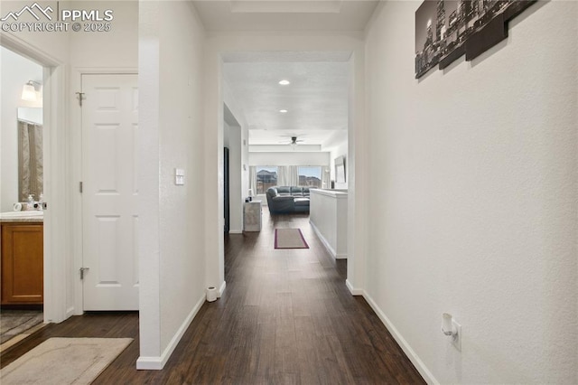 corridor with dark wood-type flooring, a sink, and baseboards