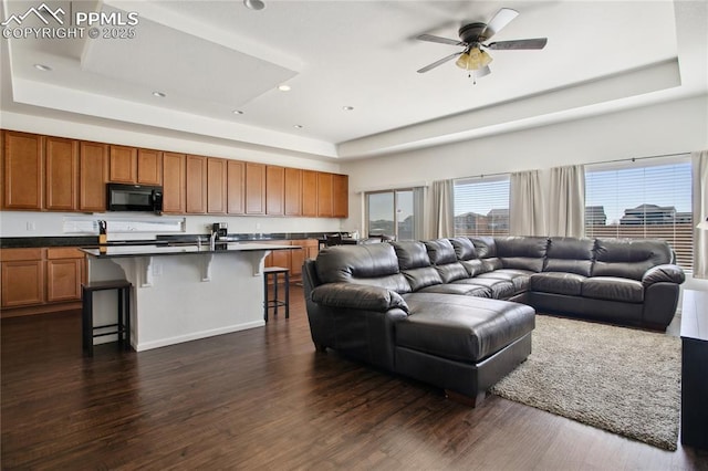 living room featuring dark wood-type flooring, recessed lighting, a raised ceiling, and a ceiling fan