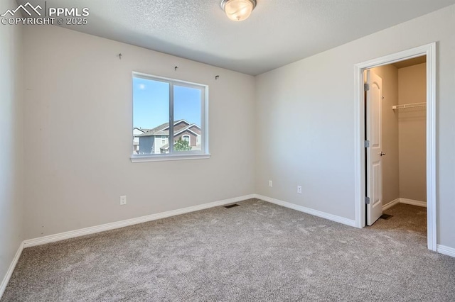 unfurnished bedroom with baseboards, carpet flooring, visible vents, and a walk in closet