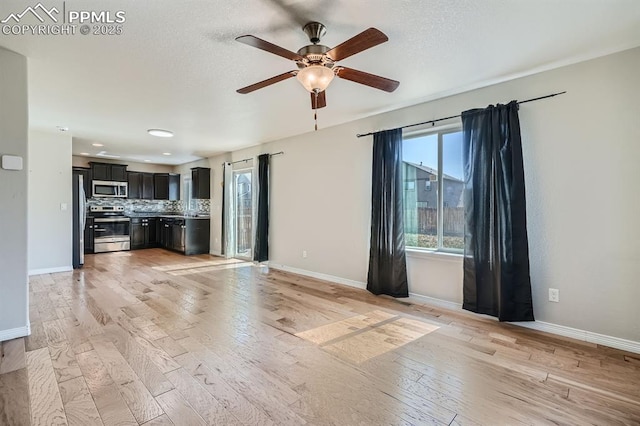 unfurnished living room with ceiling fan, a textured ceiling, light wood-type flooring, and baseboards