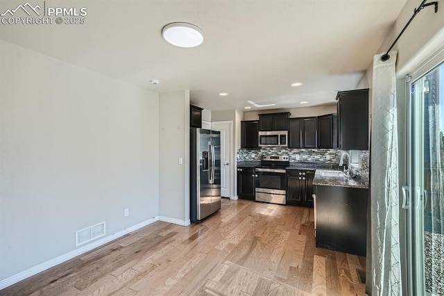 kitchen with visible vents, appliances with stainless steel finishes, dark cabinetry, light wood-type flooring, and backsplash