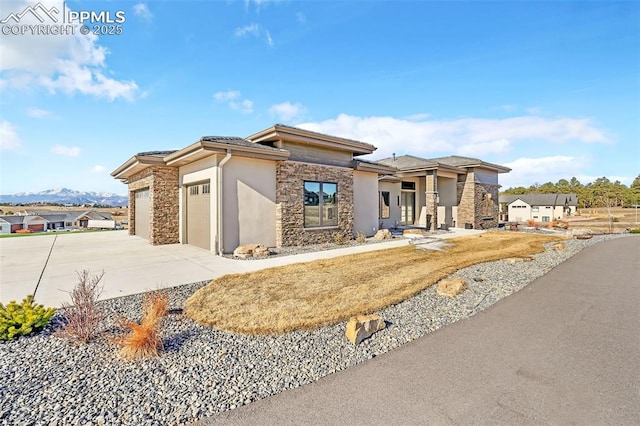 prairie-style house with a garage, driveway, stone siding, and stucco siding