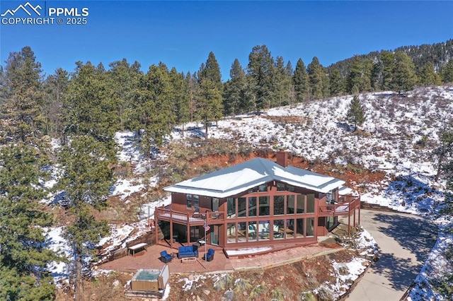 snow covered rear of property featuring a wooded view, a chimney, and a wooden deck