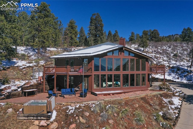 snow covered rear of property featuring a sunroom, a chimney, a deck, and a patio