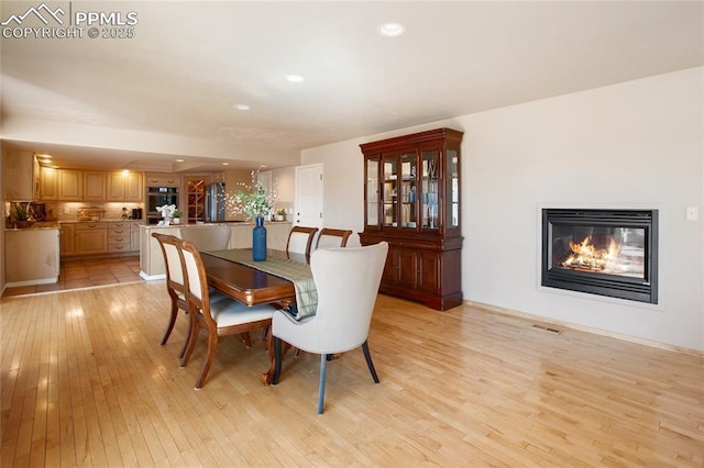 dining room featuring a glass covered fireplace, visible vents, light wood finished floors, and recessed lighting