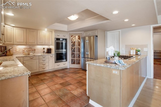 kitchen featuring stainless steel appliances, a tray ceiling, light stone counters, and tasteful backsplash