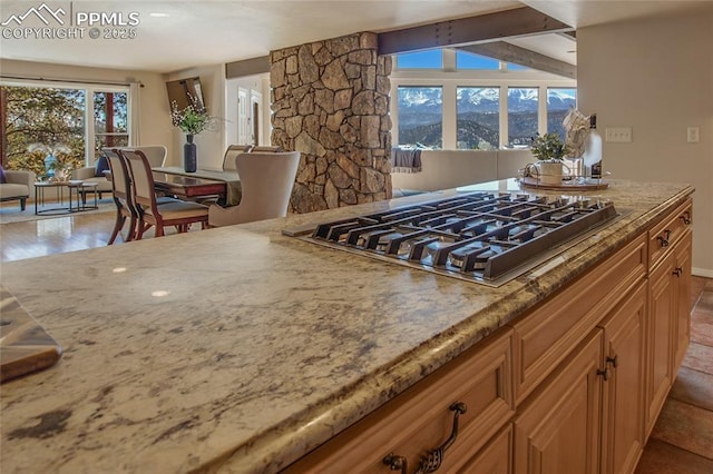 kitchen with light stone counters, stainless steel gas stovetop, and lofted ceiling with beams