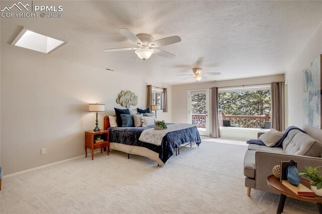 bedroom with a textured ceiling, light carpet, a skylight, a ceiling fan, and baseboards