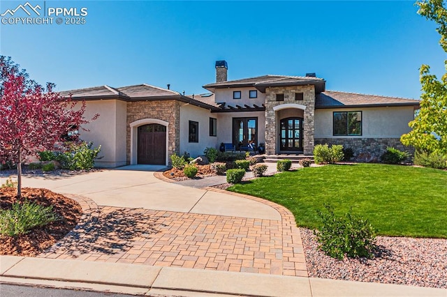 prairie-style home featuring a front yard, stucco siding, decorative driveway, a garage, and stone siding