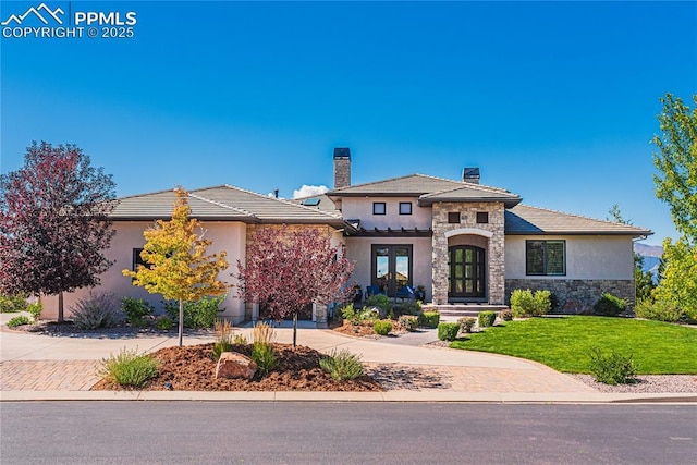 prairie-style house featuring a front lawn, decorative driveway, french doors, and stone siding