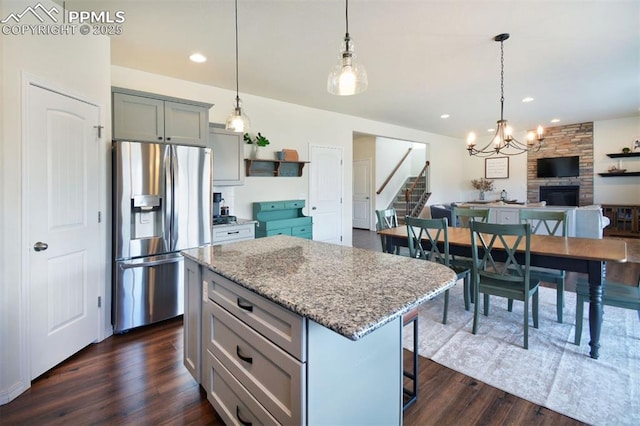 kitchen featuring a center island, light stone countertops, dark wood finished floors, pendant lighting, and stainless steel fridge