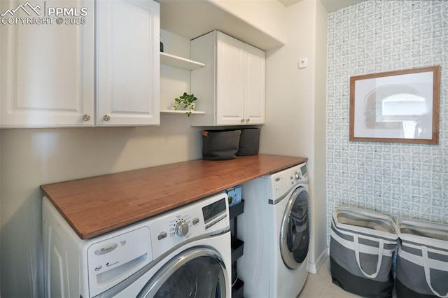 clothes washing area with washing machine and clothes dryer, cabinet space, and tile patterned floors