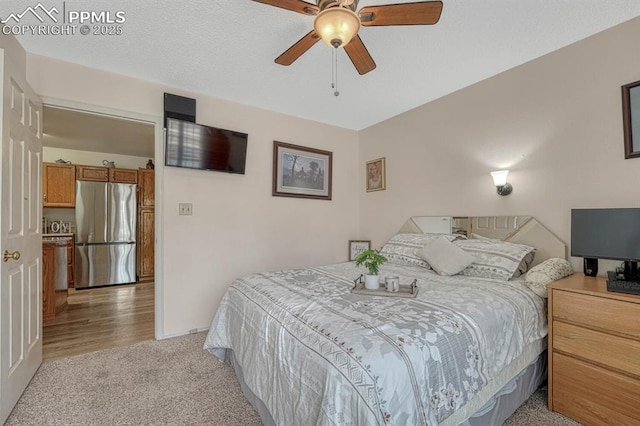 bedroom featuring a ceiling fan, freestanding refrigerator, light carpet, and a textured ceiling