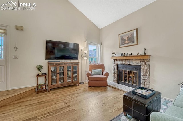 living room featuring baseboards, vaulted ceiling, wood finished floors, and a stone fireplace