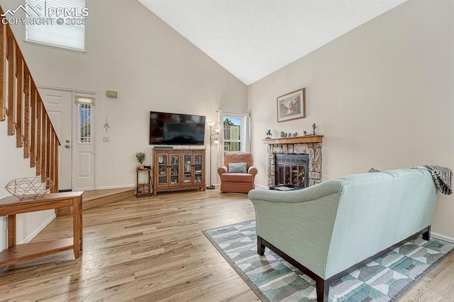 living room with a fireplace, high vaulted ceiling, light wood-type flooring, baseboards, and stairs