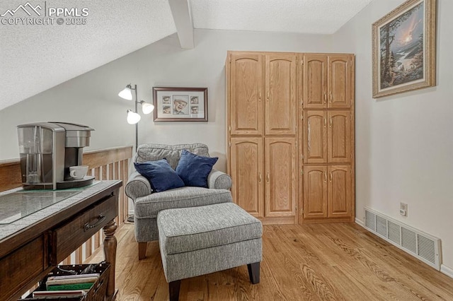 living area with visible vents, light wood-style flooring, lofted ceiling with beams, a textured ceiling, and baseboards