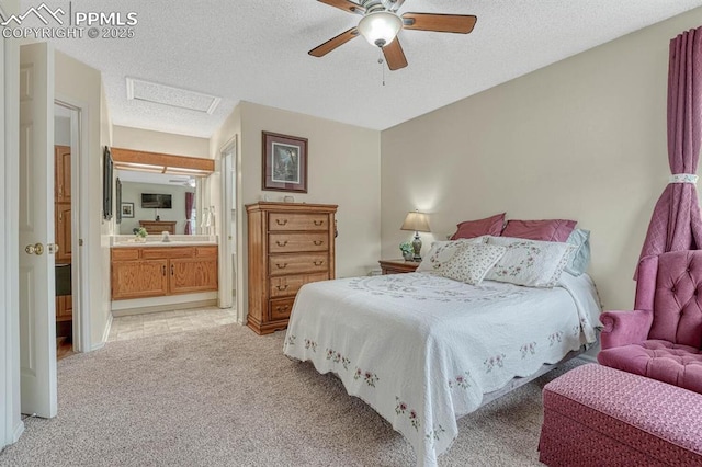 bedroom with a textured ceiling, ensuite bathroom, light carpet, a ceiling fan, and attic access