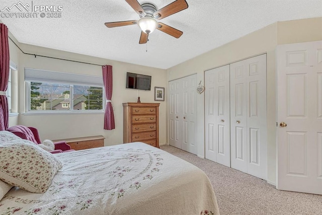 bedroom featuring a textured ceiling, carpet, two closets, and a ceiling fan