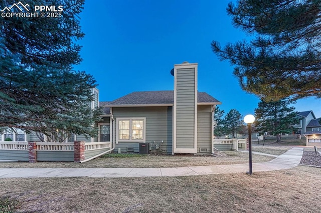 back of property featuring a shingled roof, a chimney, and central AC