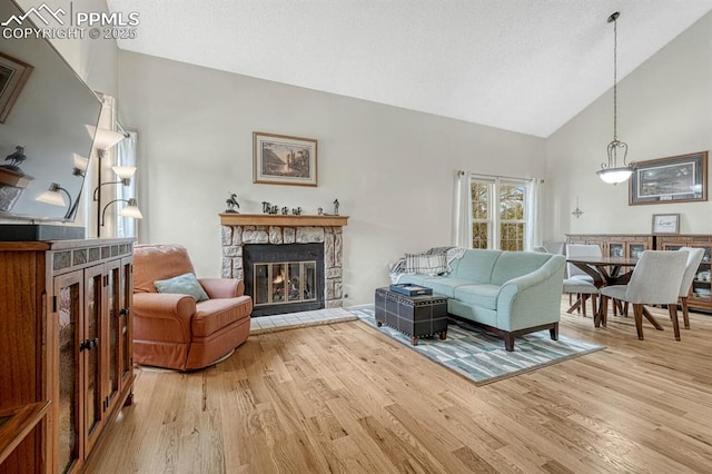 living room with high vaulted ceiling, a fireplace, a textured ceiling, and light wood finished floors