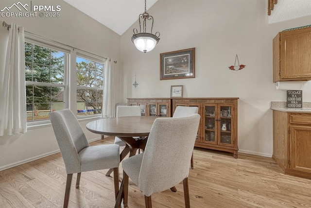 dining area featuring light wood finished floors, baseboards, and high vaulted ceiling