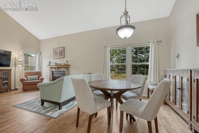 dining space featuring light wood finished floors, high vaulted ceiling, and a stone fireplace