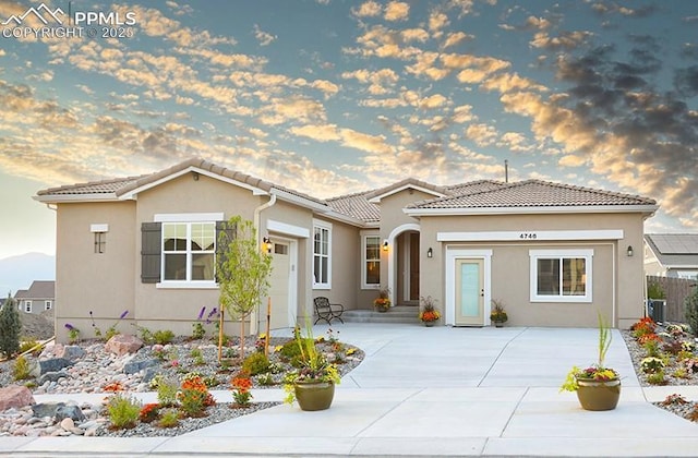 mediterranean / spanish-style house with an attached garage, a tiled roof, concrete driveway, and stucco siding