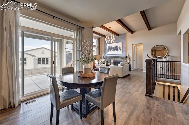 dining room featuring beam ceiling, a fireplace, wood-type flooring, visible vents, and an inviting chandelier