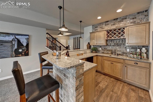 bar featuring light wood-style flooring, a sink, baseboards, hanging light fixtures, and stairway