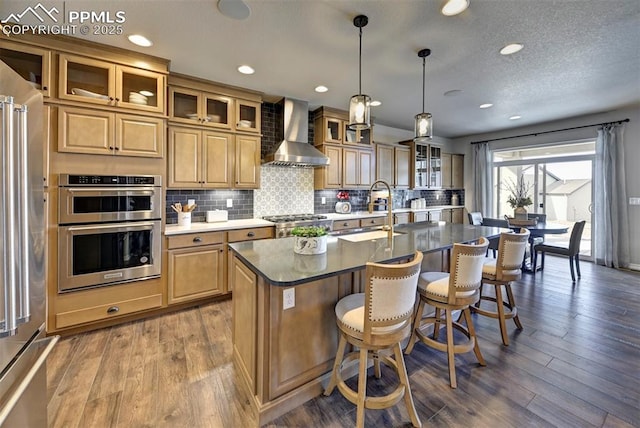 kitchen with stainless steel appliances, wall chimney range hood, a breakfast bar area, and wood finished floors