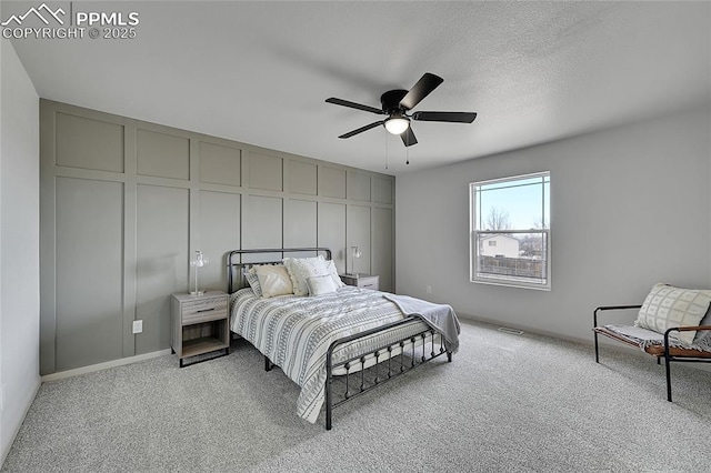 bedroom featuring ceiling fan, carpet, a decorative wall, and a textured ceiling