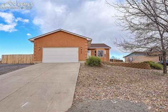 view of front of property with driveway, an attached garage, fence, and stucco siding