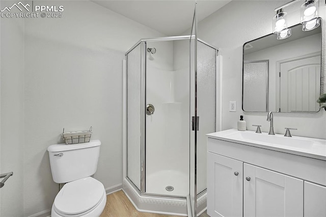 bathroom with toilet, a shower stall, vanity, wood finished floors, and baseboards