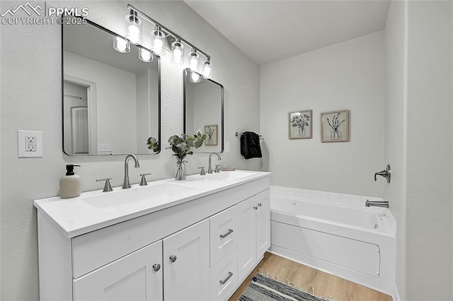 bathroom with double vanity, wood finished floors, a sink, and a bath