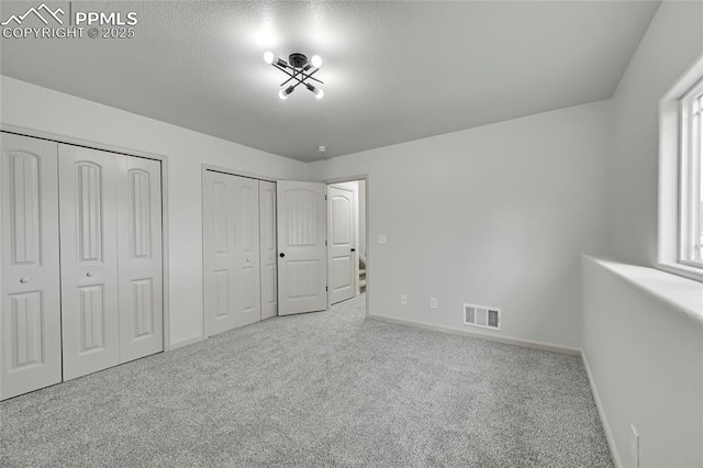 unfurnished bedroom featuring baseboards, carpet, visible vents, and two closets